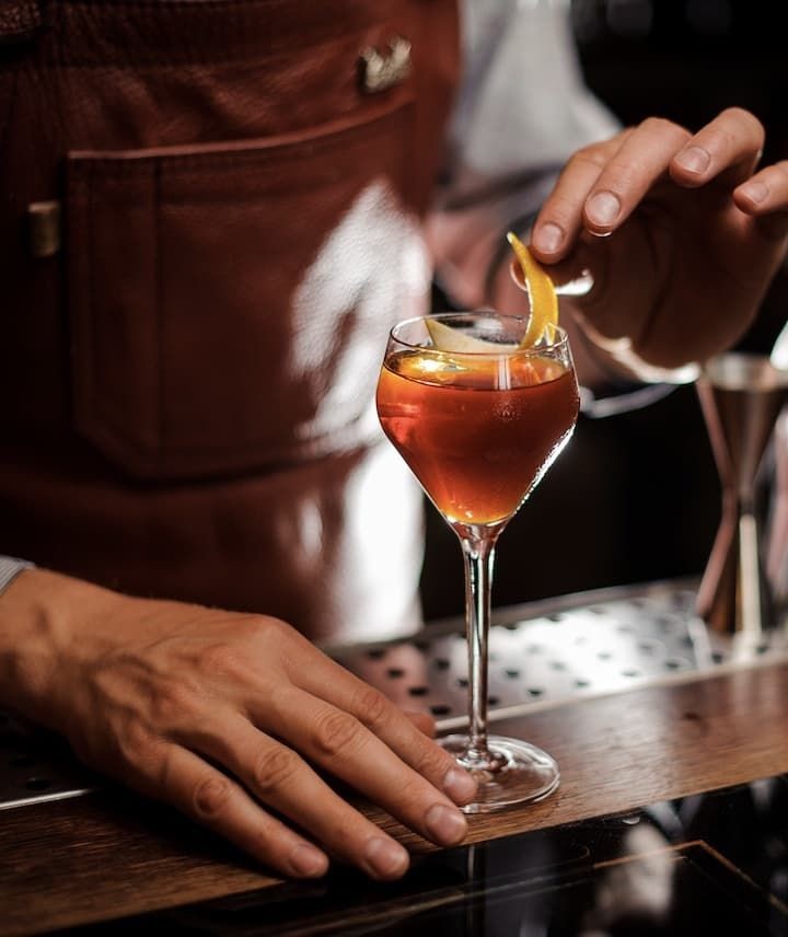 Bartender garnishing a cocktail with an orange twist at a bar counter.