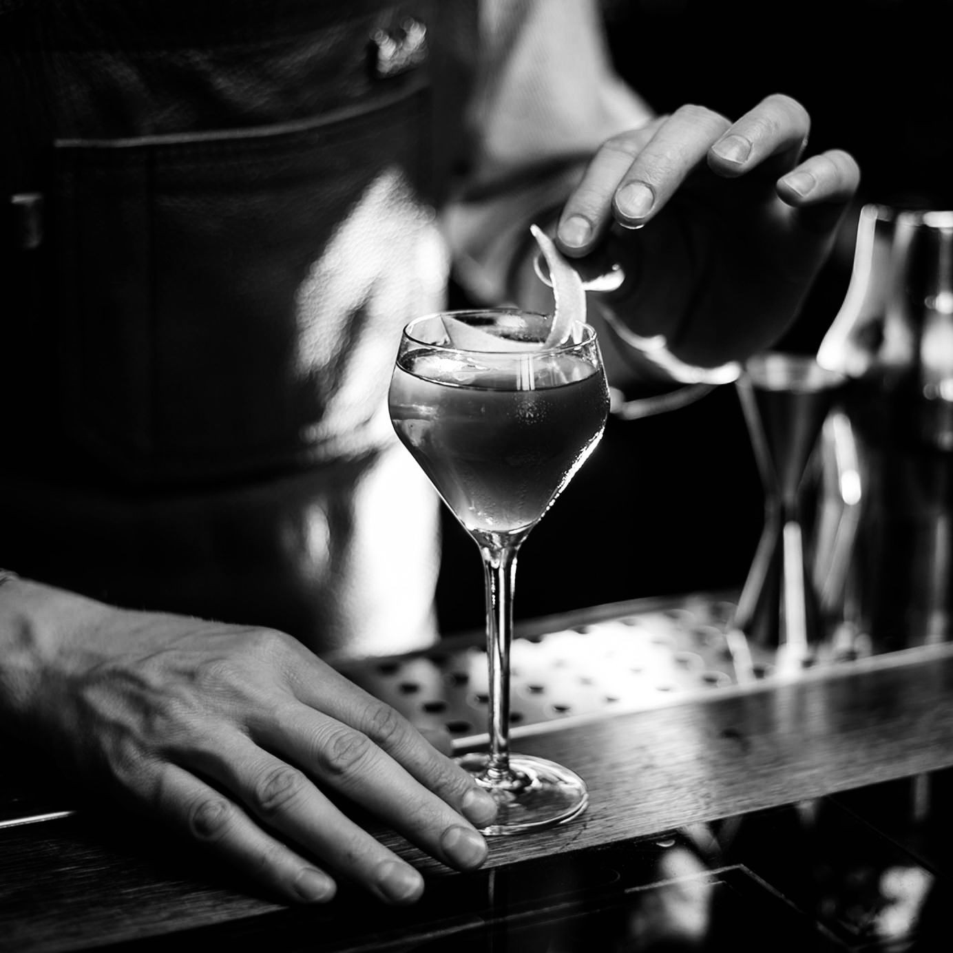 Bartender garnishing a cocktail with a peel in a dimly lit bar setting.